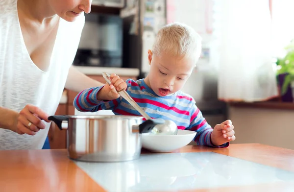 Un niño discapacitado con síndrome vertiendo sopa en un plato adentro, a la hora del almuerzo . —  Fotos de Stock