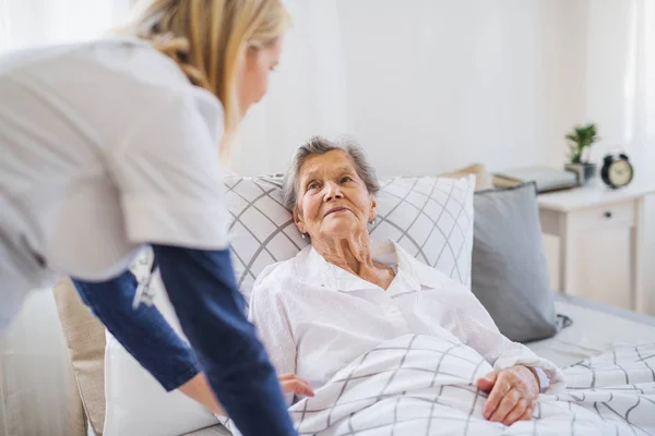 En hälsa besökare att prata med en sjuk äldre kvinna ligger i sängen hemma. — Stockfoto