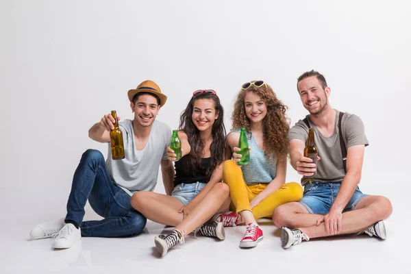 Porträt einer fröhlichen jungen Gruppe von Freunden mit Flaschen auf dem Boden in einem Atelier. — Stockfoto