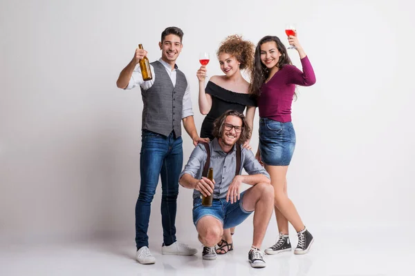 Портрет молодой группы друзей, стоящих в студии, держащих бутылки и бокалы . — стоковое фото