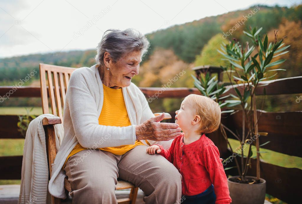 Elderly woman sitting with a toddler great-grandchild on a terrace in autumn.