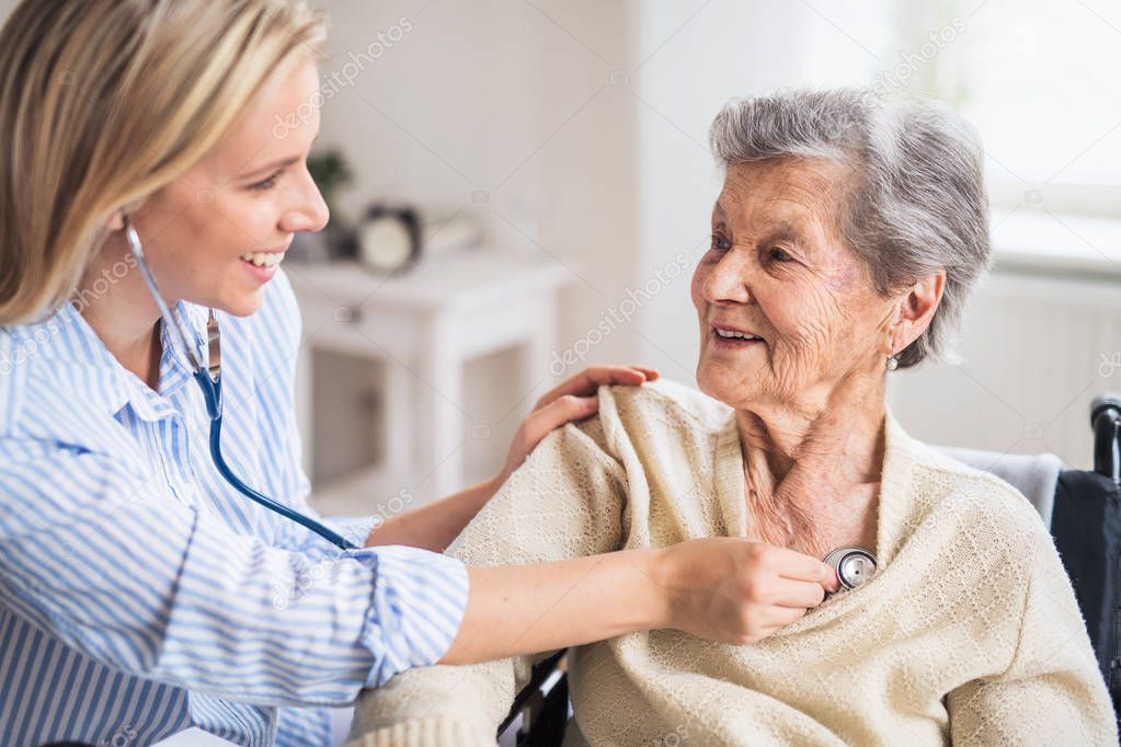 A health visitor examining a senior woman with a stethoscope at home.