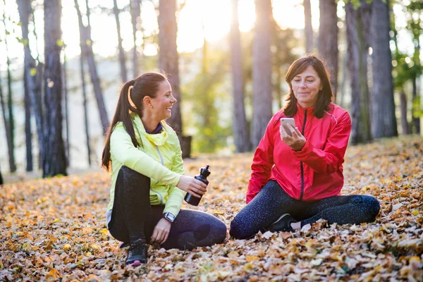 Dos corredoras femeninas con smartphone descansando al aire libre en el bosque en otoño naturaleza . — Foto de Stock