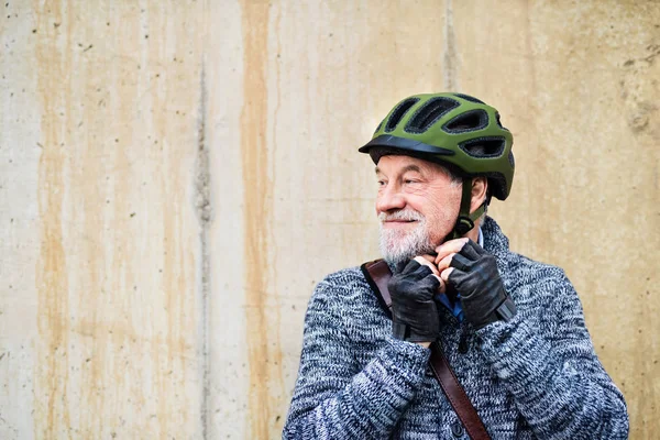 Uomo anziano attivo in piedi all'aperto contro un muro di cemento, indossando il casco da bicicletta . — Foto Stock