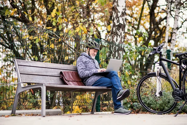 Старший человек с электровелосипедом сидит на скамейке в городе, используя ноутбук . — стоковое фото