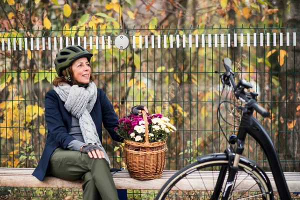 Electrobike と花の町で屋外のベンチに座っている年配の女性. — ストック写真