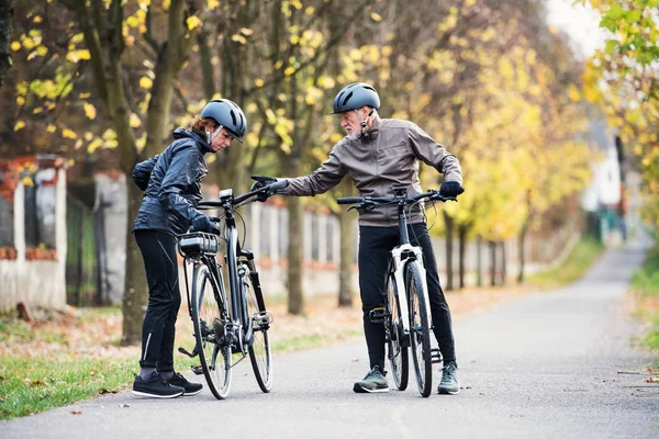 Active senior couple with electrobikes standing outdoors on a road in nature. — Stock Photo, Image