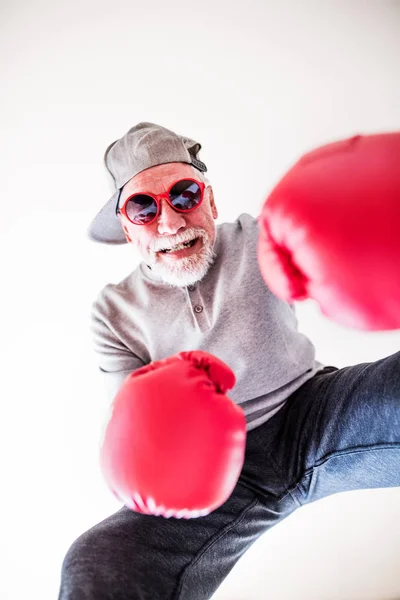 Um homem idoso com óculos de sol e luvas de boxe se divertindo em casa . — Fotografia de Stock