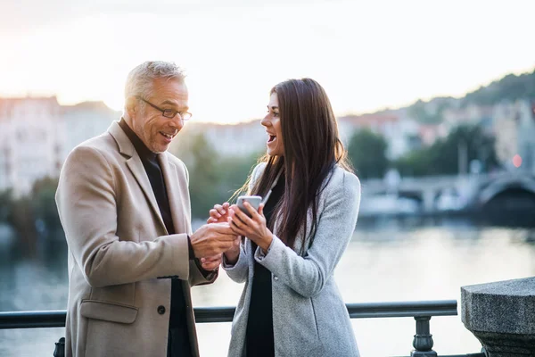 Hombre y mujer socios de negocios con smartphone de pie en la ciudad, expresando emoción . — Foto de Stock