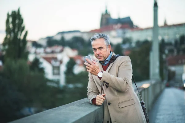 Homme d'affaires mature avec smartphone debout au bord de la rivière dans la ville de Prague, prendre selfie . — Photo