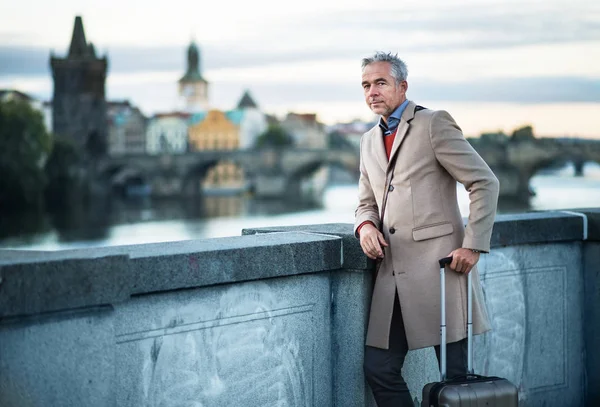 Uomo d'affari maturo con valigia in piedi su un ponte nella città di Praga . — Foto Stock