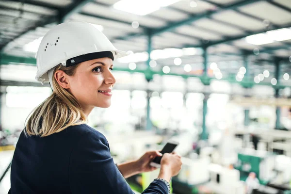 Portrét průmyslové ženy s smartphone, stojící v továrně. — Stock fotografie