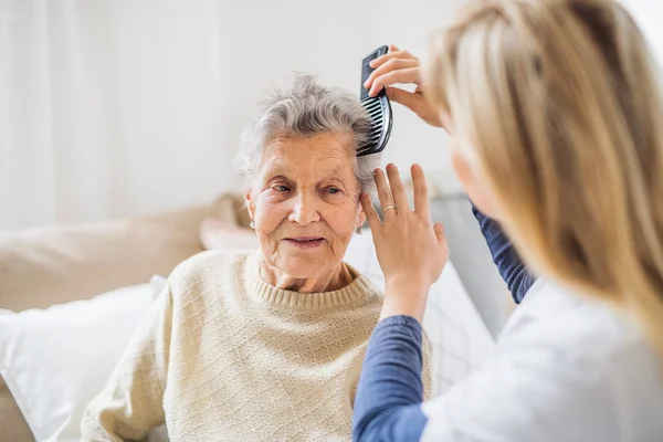 Un visitante de la salud peinando el cabello de una mujer mayor en casa .. — Foto de Stock