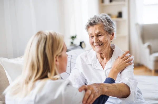 Una visita de salud hablando con una anciana enferma sentada en la cama en casa . — Foto de Stock