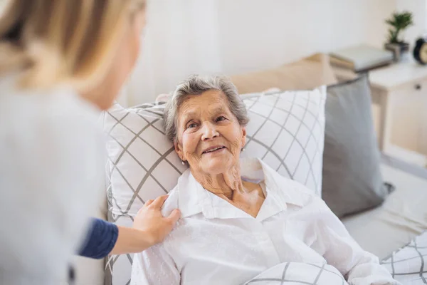 Un visitante de la salud hablando con una anciana enferma acostada en la cama en casa . —  Fotos de Stock