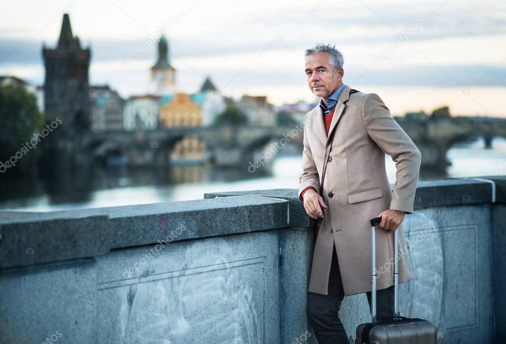 Mature businessman with suitcase standing on a bridge in Prague city.