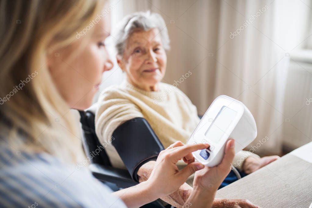 A health visitor measuring a blood pressure of a senior woman at home.