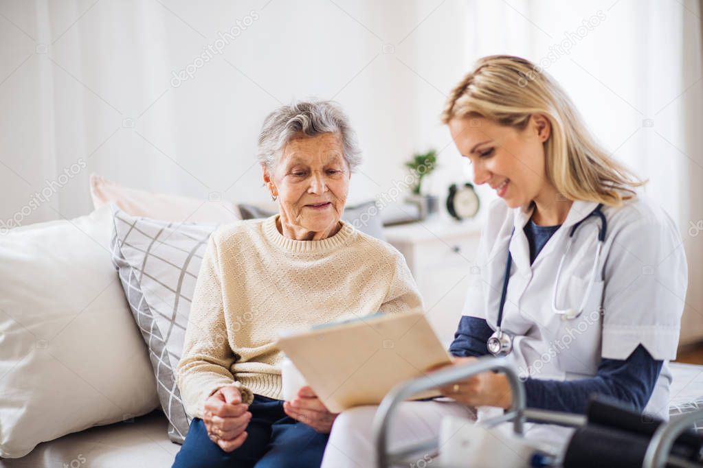 A health visitor and a senior woman sitting on a bed at home, talking.