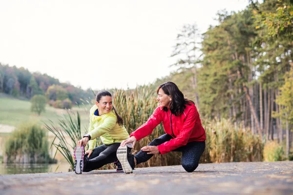 Duas corredoras do sexo feminino esticando as pernas ao ar livre no parque no outono natureza . — Fotografia de Stock