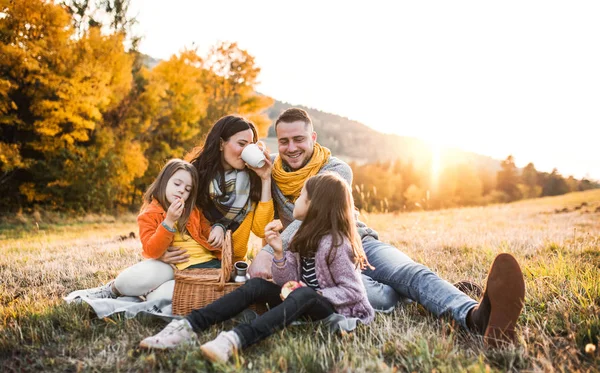 Une jeune famille avec deux jeunes enfants pique-niquer en automne nature au coucher du soleil . — Photo