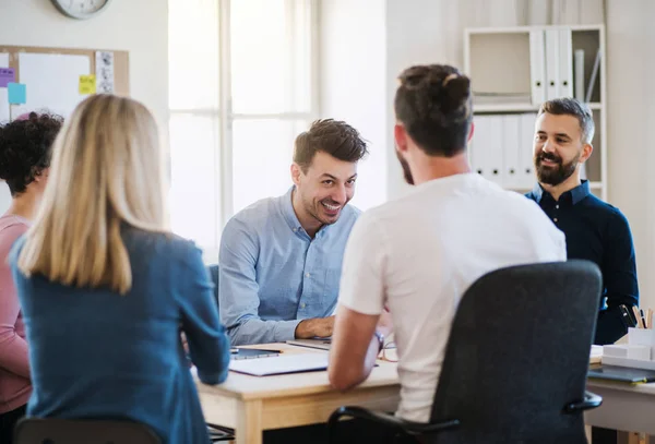 Groep van jonge ondernemers zitten rond de tafel in een modern kantoor, bijeenkomst. — Stockfoto