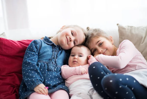 Um retrato de três meninas pequenas sentadas dentro de casa em um sofá . — Fotografia de Stock
