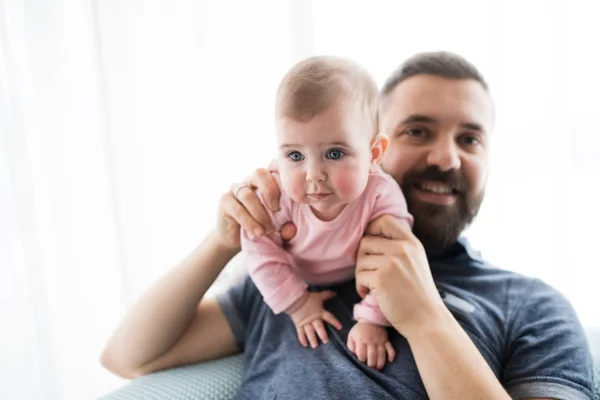 Porträt eines jungen Vaters mit kleiner Tochter, die drinnen auf einem Sofa sitzt. — Stockfoto