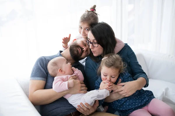 Een portret van een jong gezin met kleine kinderen binnenshuis zittend op een bank, plezier. — Stockfoto