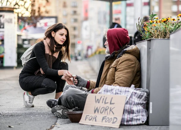 Jonge vrouw geven van geld aan dakloze bedelaar man zit in de stad. — Stockfoto