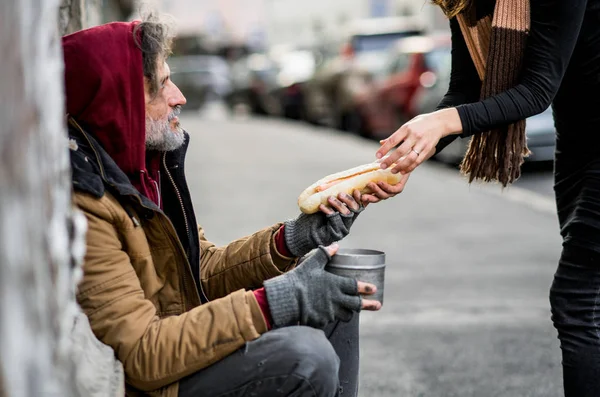 Onherkenbaar vrouw geven voedsel aan dakloze bedelaar man zit in de stad. — Stockfoto