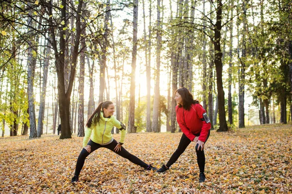 Duas corredoras do sexo feminino que se estendem ao ar livre na floresta no outono natureza . — Fotografia de Stock