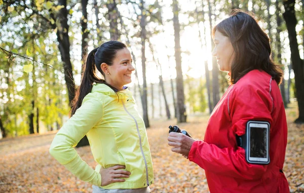 Zwei Läuferinnen mit Smartphone ruhen sich im Wald in herbstlicher Natur aus. — Stockfoto