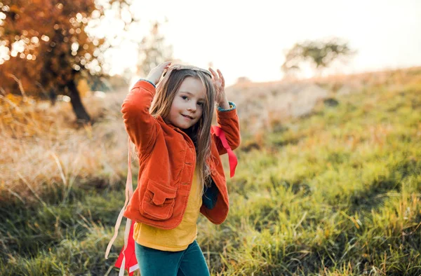 A small girl playing with a rainbow hand kite in autumn nature at sunset. — Stock Photo, Image