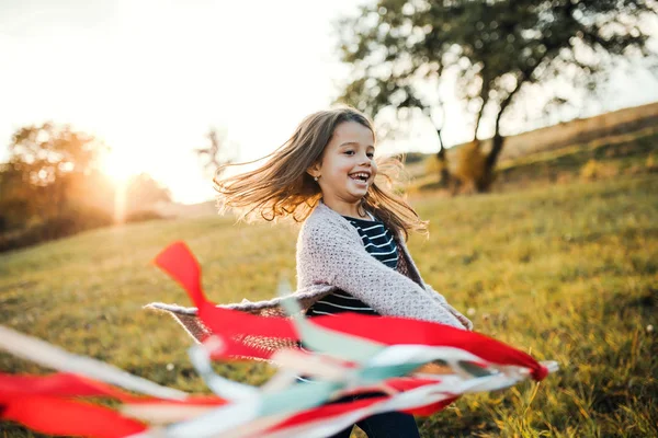 Una niña pequeña jugando con una cometa de la mano del arco iris en la naturaleza del otoño al atardecer . — Foto de Stock