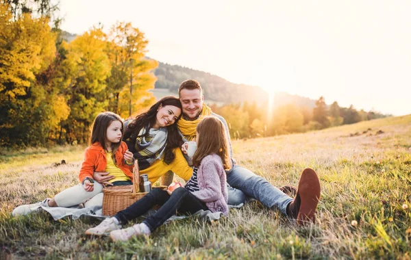 Μια νεαρή οικογένεια με δύο μικρά παιδιά έχοντας πικνίκ φθινόπωρο φύσης στο ηλιοβασίλεμα. — Φωτογραφία Αρχείου