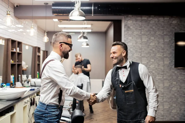 Hipster homme client serrant la main avec coiffeur et coiffeur dans le salon de coiffure . — Photo