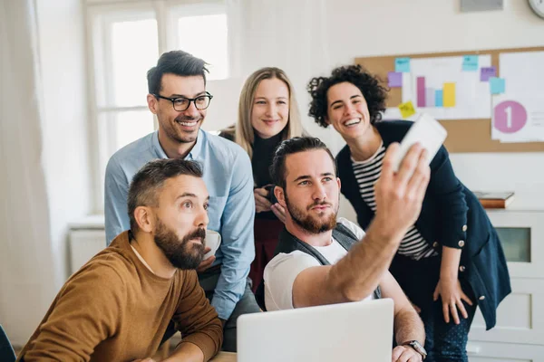 Group of young businesspeople with smartphone in office, taking selfie.