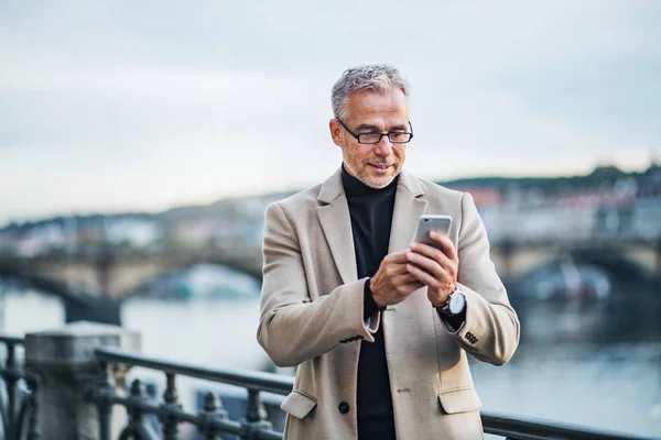 Зрелый бизнесмен со смартфоном, стоящим у реки в Праге, делает селфи . — стоковое фото