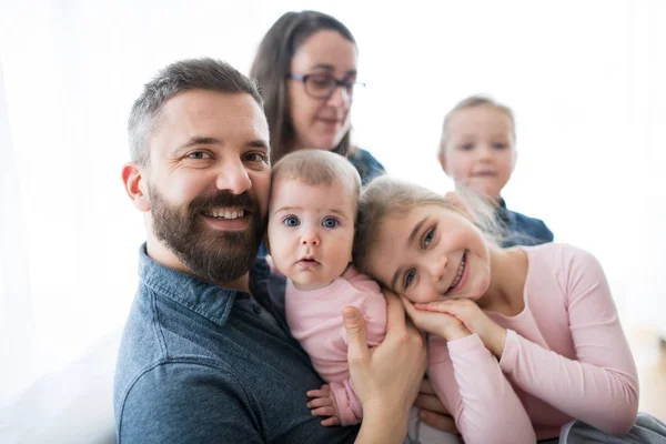 Portrait d'une jeune famille avec de jeunes enfants assis à l'intérieur sur un canapé . — Photo