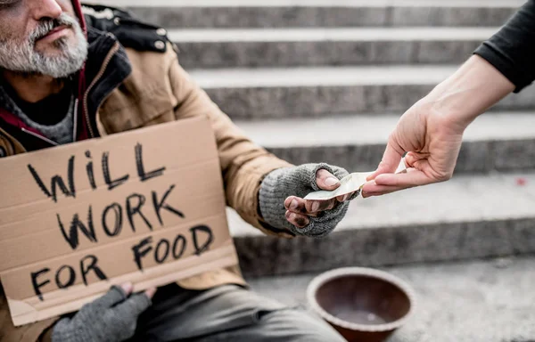 Brzuch kobiety dając pieniądze, aby człowiek bezdomny żebrak siedzący w mieście. — Zdjęcie stockowe