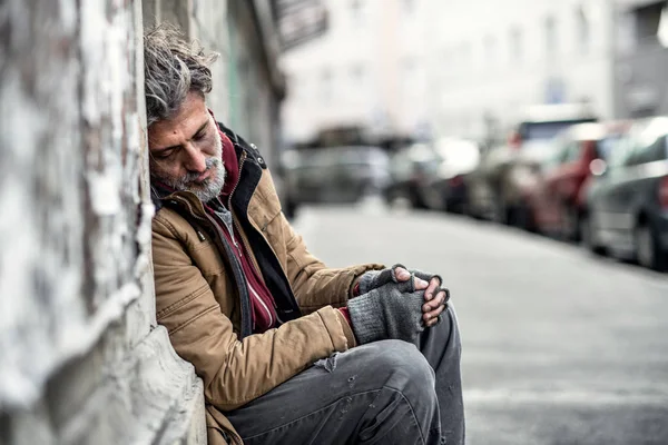 Hombre mendigo sin hogar sentado al aire libre en la ciudad pidiendo una donación de dinero, durmiendo . — Foto de Stock