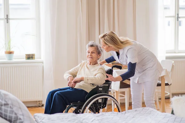 Un visiteur de la santé parle à une femme âgée en fauteuil roulant à la maison . — Photo