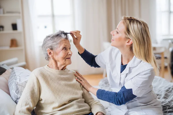 Un visitante de la salud peinando el cabello de una mujer mayor en casa .. — Foto de Stock