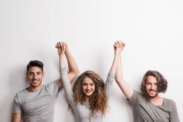 Ritratto di giovane ragazza gioiosa con due amici maschi in piedi in uno studio, mani alzate . — Foto Stock