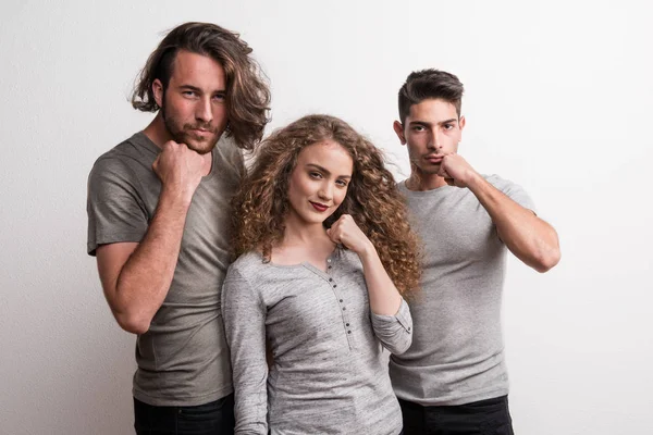 Retrato de una joven alegre con dos amigos varones de pie en un estudio, puño contra rostro . — Foto de Stock