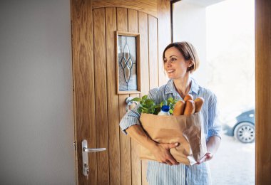 Kağıt alışveriş çantası ön kapıdan yürüyerek yiyecek olan bir genç kadın.
