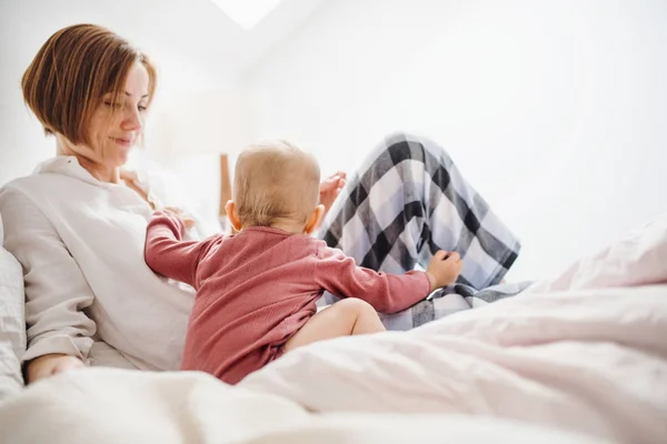 O mamă tânără cu o fiică mică stând în pat dimineața, jucându-se . — Fotografie, imagine de stoc