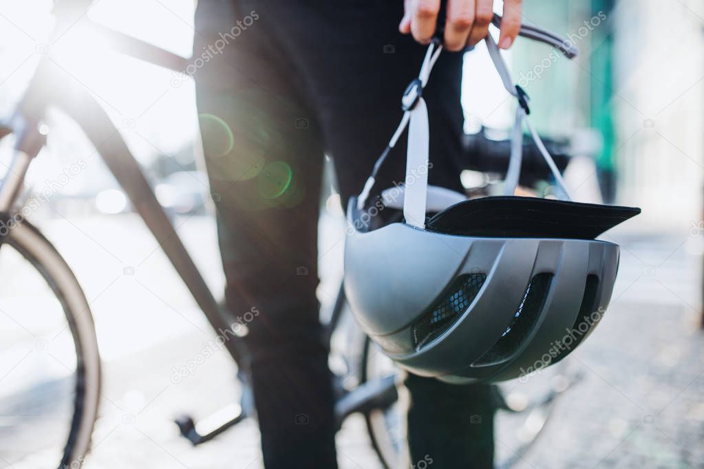 Midsection of man commuter or courier with electric bicycle and helmet in city.