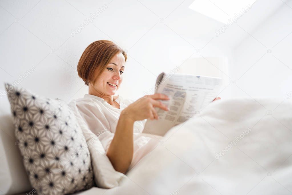 A young woman reading newspapers in bed in the morning in a bedroom.