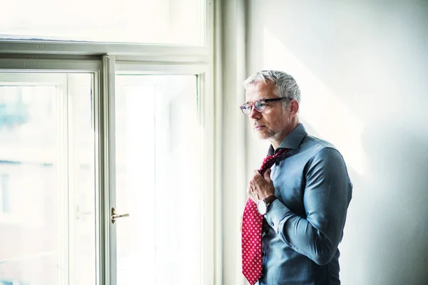 Rijpe zakenman op een zakelijke reis staande in een hotelkamer, aankleden. — Stockfoto